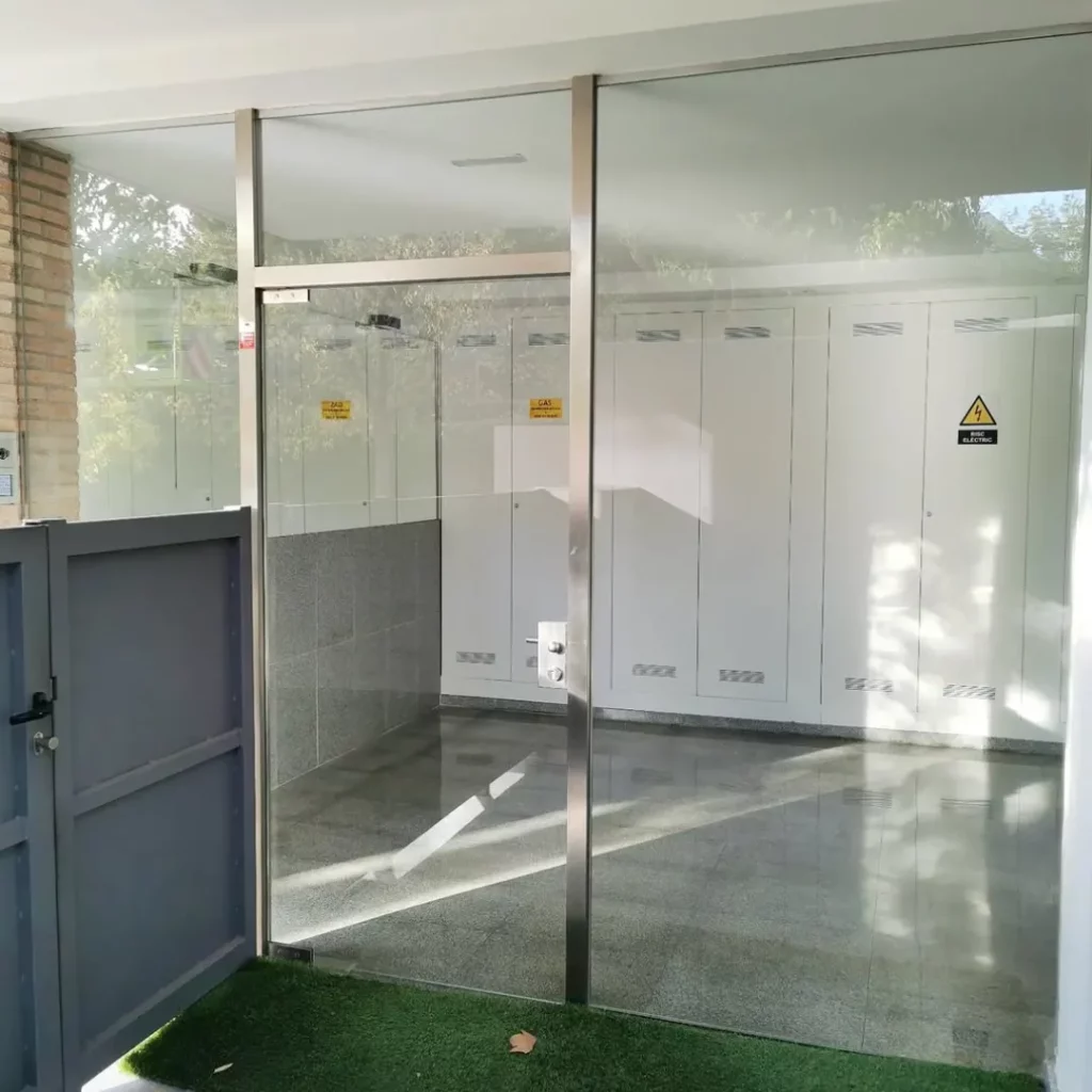 Acceso comunitario acristalado con puerta de vidrio y perfilería de acero inoxidable