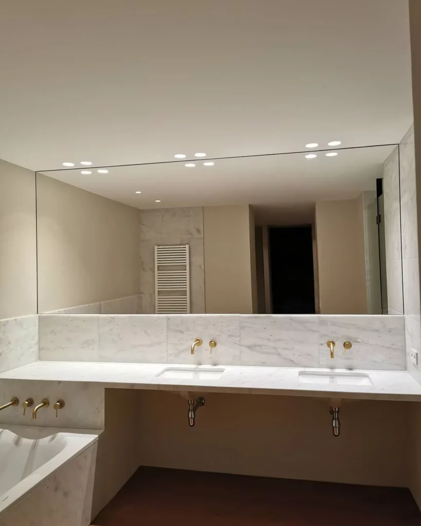 Espejo de pared a pared sobre encimera de mármol con doble lavabo