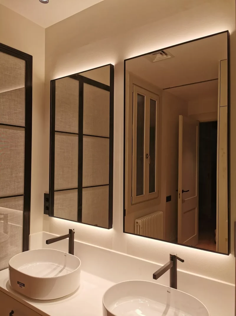 Espejos con marco negro y retroiluminación LED cálida sobre doble lavabo